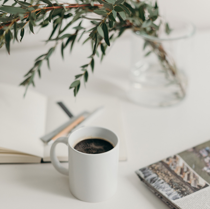 Coffee mug on a desk with flower and notebook.